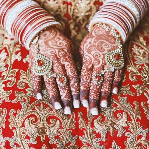 The close-up shot of Indian bride with beautiful pink saree showing mehndi (henna) hand with a lot of glitter bracelets (bangles) on her wrist